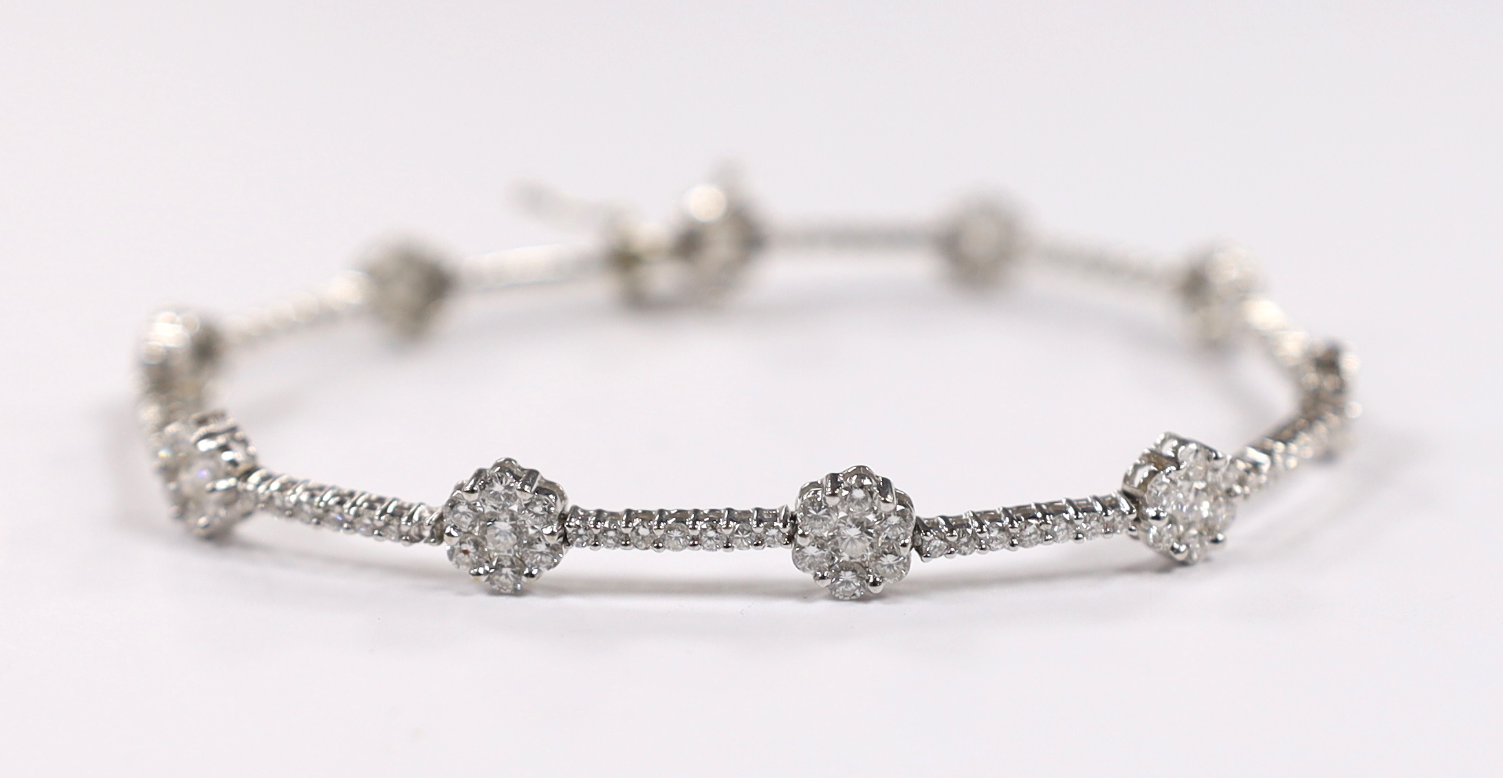 A modern 18k white metal and diamond cluster set flower head line bracelet, 17.5cm, gross weight 8.4 grams.